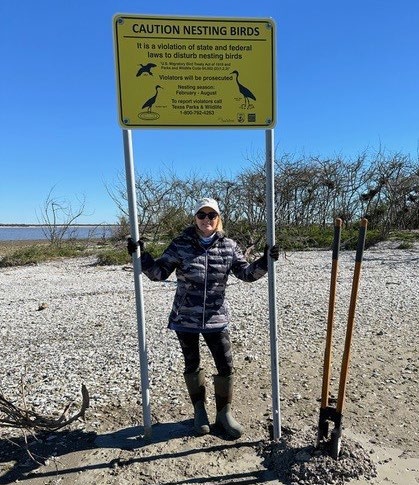 woman with yellow sign above her with nesting bird information beach in background