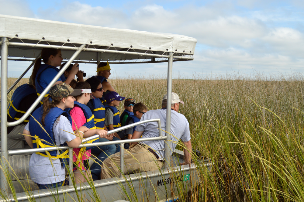 kids and an adult on a boat in marsh grass
