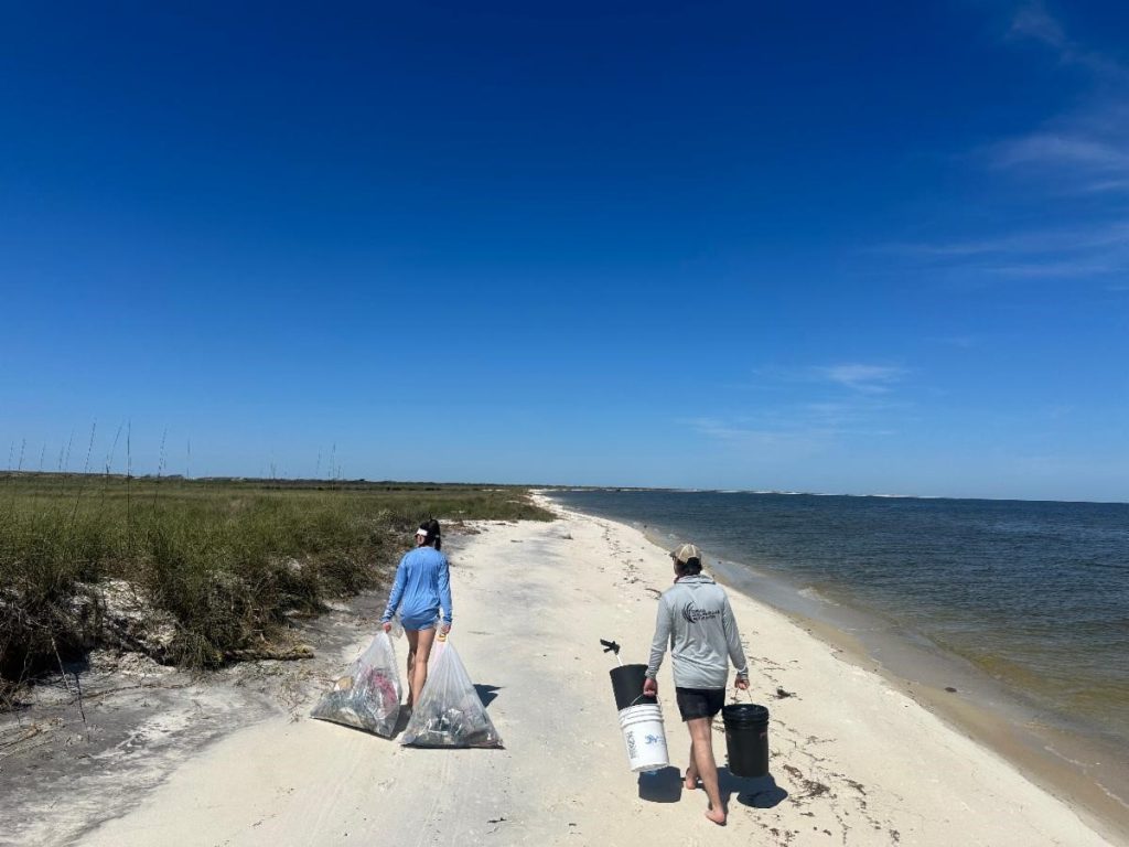 Two people walk down a beach collecting trash