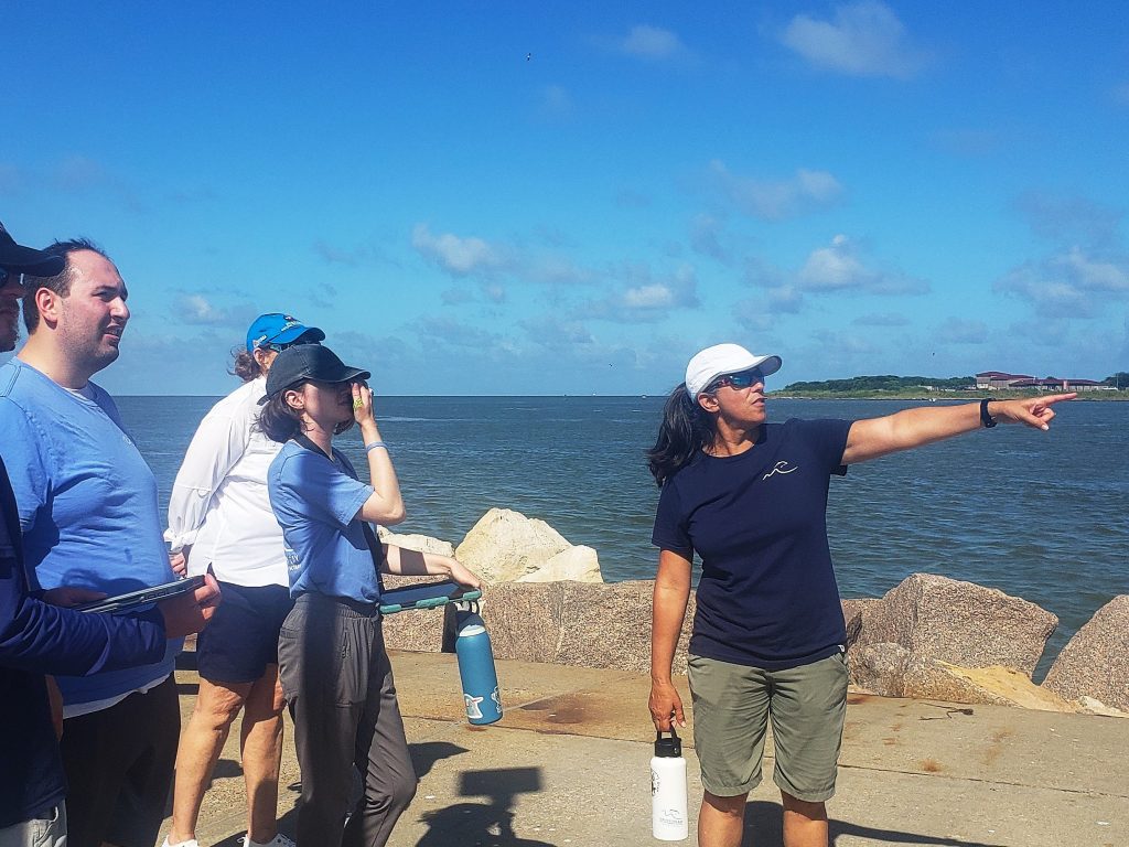 several people standing near water. One in dark blue is pointing.